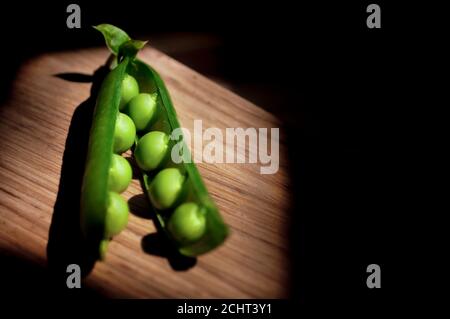 Pea pod aperto nei raggi di luce, il resto della foto in ombra, un luogo per il testo Foto Stock