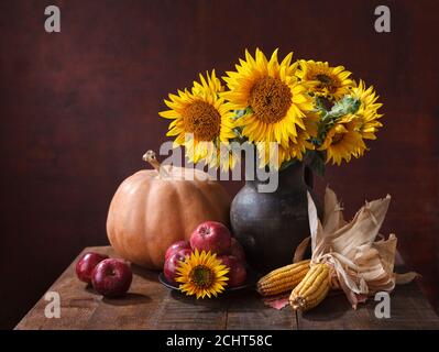 Autunno ancora vita con zucca, cornetti, mele e bouquet di girasoli in pentola di argilla su vecchio tavolo di legno. Foto Stock