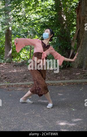 Circondato da alberi e fogliame, un grazioso ballerino cinese americano danzano alla musica folk tradizionale. I un parco a Queens, New York City Foto Stock