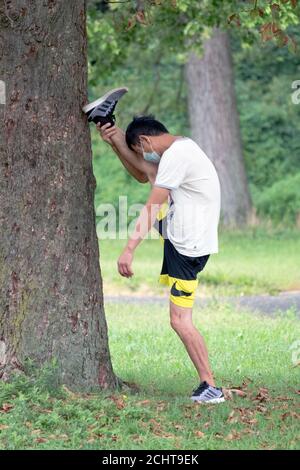 Un corridore asiatico-americano snello fa un po' di stretching estremo mentre si riscalda per una corsa. In un parco a Queens, New York City. Foto Stock