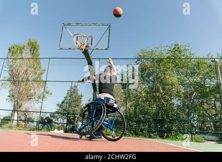 Uomo in sedia a rotelle che gioca a basket Foto Stock