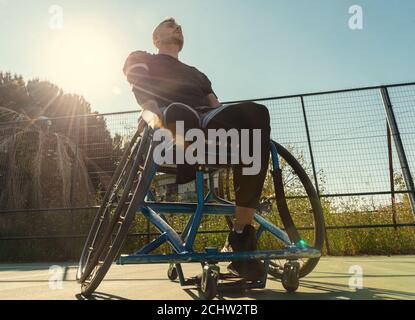 Giovane bell'uomo in sedia a rotelle al campo da gioco di basket Foto Stock