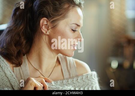 giovane donna rilassata in accogliente cardigan lavorato a maglia nel moderno soggiorno nel soleggiato giorno d'autunno. Foto Stock