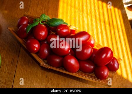 Piccoli pomodori rossi in cestino su un tavolo di legno, fuoco selettivo Foto Stock