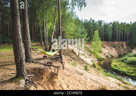 Vista panoramica della ripida riva del fiume, l'acqua e la foresta in distance.A uomo ыдуузштп in un'amaca Foto Stock