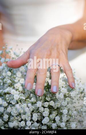 Sposa mano con anello di nozze poggiato su fiori. Foto Stock