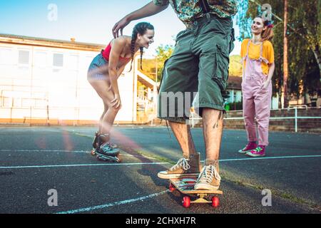 Ragazzo teenager sullo skate con due ragazze dietro di lui che si acclamano e ridendo Foto Stock