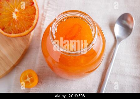 Marmellata d'arancia e di kumquat in un vaso di vetro con frutta fresca su una tovaglia di lino bianco. Fatto in casa, primo piano. Foto Stock
