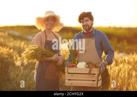 Vita in su ritratto della coppia matura sorridente che tiene raccolto ricco mentre si sta in piedi in campo d'oro illuminato dalla luce del tramonto, copia spazio Foto Stock