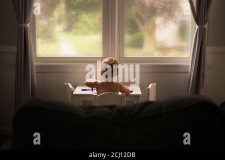 Bambino seduto a una scrivania bianca di fronte alle finestre Colorazione con marcatori Foto Stock