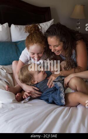 Madre e i bambini giovani si coccolano e giocano insieme su un Letto Foto Stock