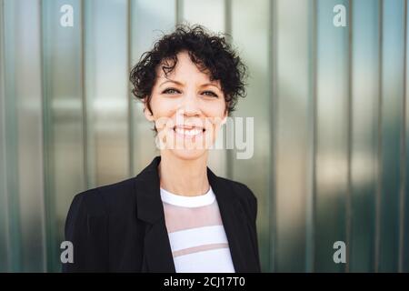 Primo piano ritratto di sorridente donna d'affari matura in tuta in piedi contro parete verde Foto Stock