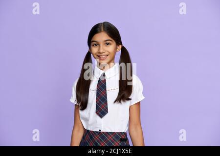 Sorridente ragazza indiana bambino indossare scuola uniforme stand su sfondo lilla, ritratto. Foto Stock
