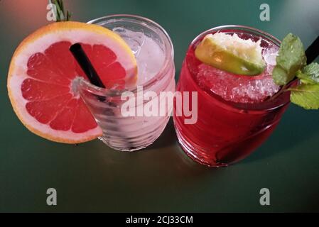 due rinfrescanti bevande alcoliche ben guarnite in bicchieri rotondi di vetro con fette di arancia e lime e menta con paglia Foto Stock