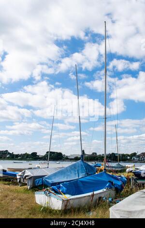 Piccole barche a vela o da pesca a terra con alberi e coperture in Mudeford Quay, Inghilterra meridionale, bellissimo cielo blu nuvoloso, molti dingy memorizzati su Foto Stock