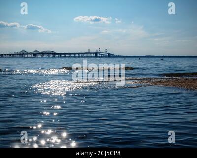 Il Cheseapeake Bay Bridge in silhouette, visto dalla costa orientale del Maryland, con acque scintillanti e gente silhouette che guadi e pesca fa Foto Stock