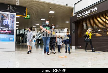 Gli acquirenti indossano maschere facciali nel tentativo di ridurre la diffusione di Coronavirus durante la pandemia del 2020 al Gateshead Metrocentre, mentre un ragazzo guarda un bac Foto Stock