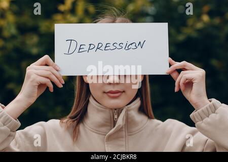 Donna che tiene foglio bianco carta etichettato parola depressione in mano. Foto Stock