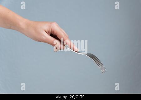 donna mano che tiene forchetta su sfondo grigio. Mangiare gesto. Foto Stock