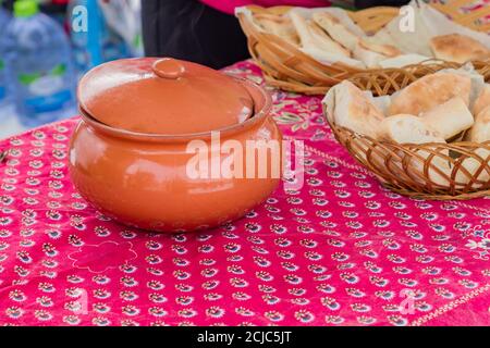 primo piano di ciotola di argilla e cesto con pita sul tavolo, all'aperto Foto Stock