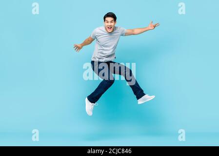 Energico felice giovane asiatico in studio di salto vestiti casual scatto isolato su sfondo azzurro