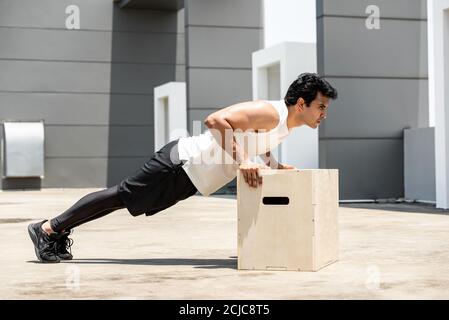 Bell'uomo sportivo indiano che fa spingere in su l'esercizio all'aperto sul tetto della costruzione, allenamento domestico nel concetto di aria aperta Foto Stock