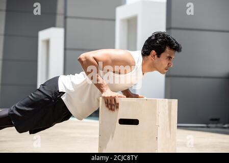 Bell'uomo sportivo indiano che fa spingere in su l'esercizio all'aperto sul tetto della costruzione, allenamento domestico nel concetto di aria aperta Foto Stock