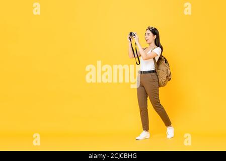 Giovane donna turistica asiatica che scatta foto con la fotocamera isolata sfondo giallo Foto Stock