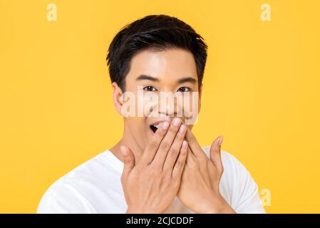 Primo piano ritratto di un giovane asiatico sorpreso con le mani bocca di copertura isolata su sfondo giallo studio Foto Stock