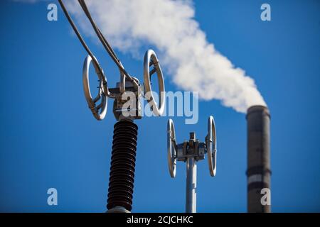 Sottostazione elettrica. Apparecchiature ad alta tensione su cielo blu. Primo piano. Fumo camino di fabbrica sfocato su sfondo. Foto Stock