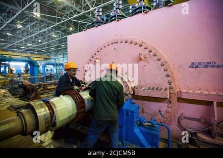 Centrale elettrica. Due operatori che fissano il generatore elettrico rosa in officina. Foto Stock