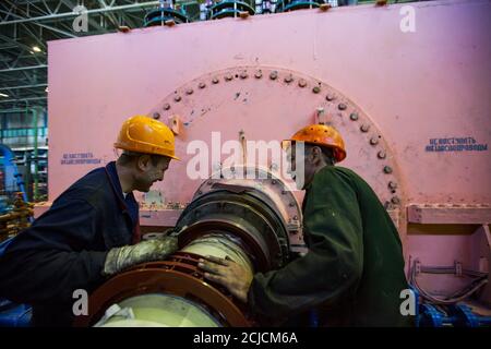 Centrale elettrica. Due operatori che fissano il generatore elettrico rosa in officina. Foto Stock