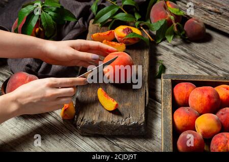 Pesche frutti interi con foglie, pesche a metà, fette di pesca su tavola di legno. Il processo di preparazione della marmellata di pesche, cucinando il dessert di pesche su rustico Foto Stock
