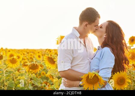 L'uomo e la donna baciano dolcemente sulla natura. Ritratto di una giovane coppia, amanti giovane uomo e donna baciando in un campo primo piano di girasoli fioriti. Foto Stock