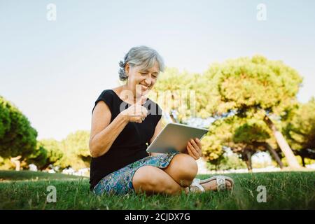 Donna anziana che parla on-line con il suo tablet in un parco Foto Stock
