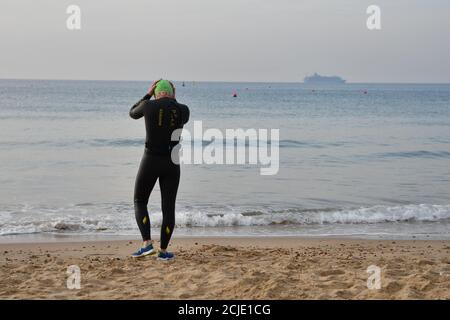 Nuotatore di mare in una muta da bagno che si prepara ad entrare in acqua. Boscombe, Bournemouth, Dorset, Regno Unito, settembre 2020. Foto Stock