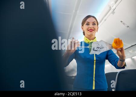 Sorridente padrona di casa dell'aria che dimostra come usare le maschere di ossigeno per volare decollo Foto Stock