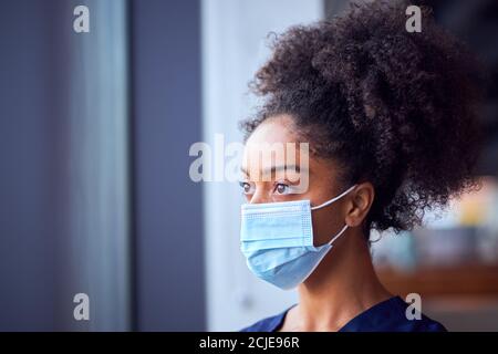 Femmina Dottore in maschera di faccia indossare scrub sotto pressione dentro Ospedale occupato durante Pandemic di salute Foto Stock