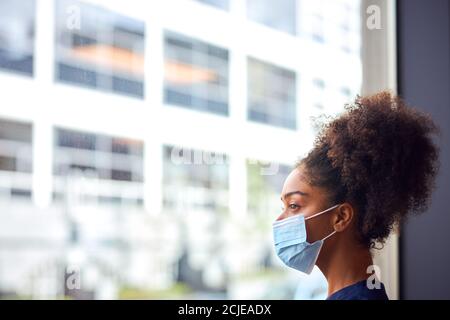 Femmina Dottore in maschera di faccia indossare scrub sotto pressione dentro Ospedale occupato durante Pandemic di salute Foto Stock