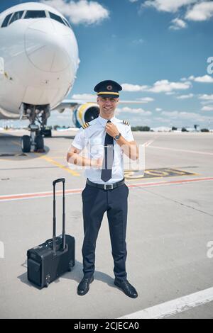 Bel pilota maschio che regola il suo legame all'aeroporto Foto Stock