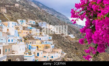 Bougainvillea luminosa e colorata con tradizionale villaggio greco su un pendio di collina con Cappella Bianca, Olympos, Karpathos, Grecia Foto Stock