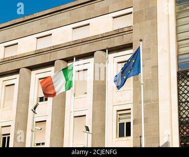 Bandiera dell'Unione europea e bandiera italiana che ondolano insieme al vento all'esterno di un edificio Foto Stock