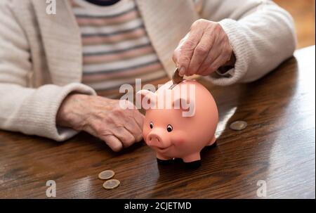 Donna anziana che mette una moneta in una banca piggy Foto Stock