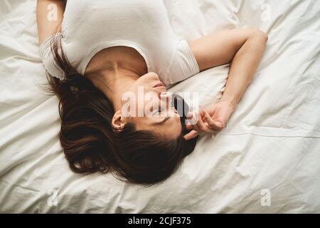 Signora calma in una t-shirt sdraiata a letto Foto Stock