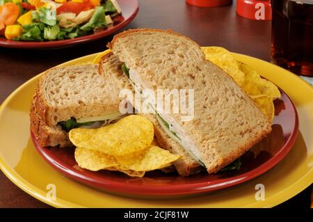 Un panino di tacchino e formaggio svizzero su pane integrale con insalata tropicale e patatine di tortilla Foto Stock