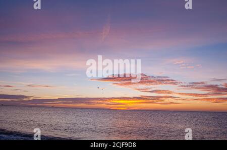 Alba sul mare con i colori che tremolano attraverso le nuvole punteggiate e un gregge di uccelli che sorvolano. Foto Stock