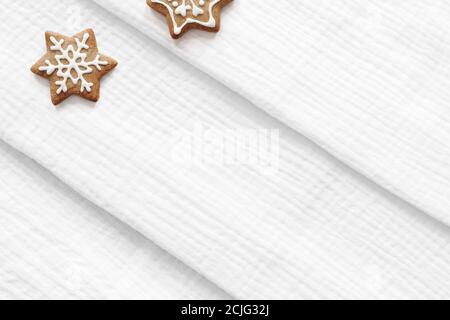 Scena di mockup in tessuto natalizio. Closeup di tessuto di cotone di mussola piegato bianco. Biscotti di pan di zenzero a forma di stella con glassa decorativa di zucchero. Vacanze Foto Stock