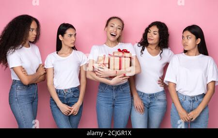 Donne invidiose guardando amico con molti regali, sfondo rosa Foto Stock