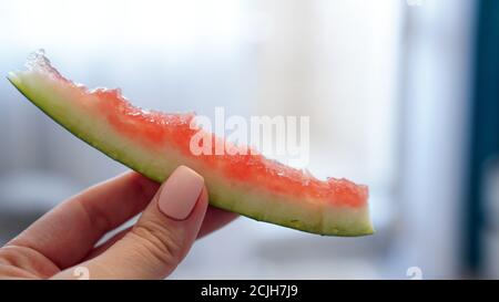 Mano tenendo mangiato fetta di anguria su sfondo chiaro sfocato Foto Stock