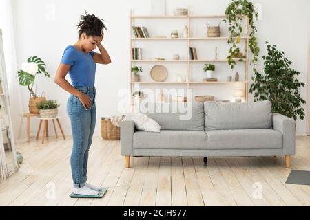 Triste ragazza africana in piedi su scale che si pesa a casa Foto Stock